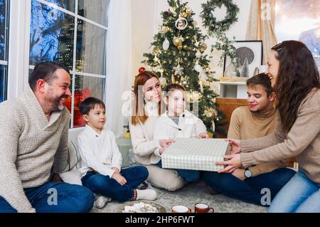 Große glückliche Familie mit Kindern, die sich zu Hause um den Weihnachtsbaum versammeln. Fröhliche Eltern, Großeltern und kleine Kinder tauschen Weihnachtsgeschenke aus Stockfoto