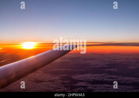 Flügelansicht des Flugzeugs, das über den Wolken am Himmel bei Sonnenuntergang fliegt Stockfoto