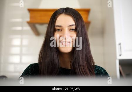 Glückliche weiße Frau, die vom Computerbildschirm liest. Schöne junge Frau, die zu Hause mit einem laptop Lächeln am Laptop arbeitet. Fröhliche Brünette im Jahr 20s tun DIS Stockfoto