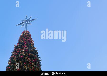 Nahaufnahme eines riesigen Weihnachtsbaums mit Sternendeko auf blauem Himmel im Hintergrund und Kopierbereich, Weihnachtsereignis für den Countdown zum neuen Jahr Stockfoto