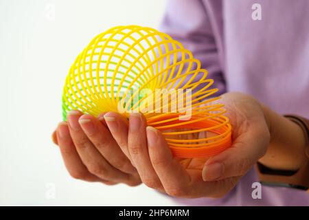 Frau spielt mit neunziger Jahren magischen Frühling Spielzeug, Kunststoff dehnbaren Regenbogen in der Hand, um Stress auf weißem Hintergrund zu lindern oder zu reduzieren. Stockfoto