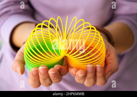 Frau, die mit dem magischen Frühlingsspielzeug der neunziger Jahre spielt, dehnbarer Regenbogen aus Kunststoff in der Hand, um Stress zu lindern oder zu reduzieren. Junge Frau mit Unterhaltungsidee. Stockfoto
