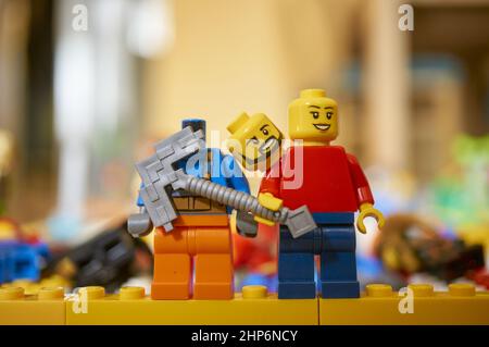 Eine LEGO-Spielzeugfigur mit einer Axt, die neben einem kopflosen Mann auf einem verschwommenen Hintergrund steht Stockfoto