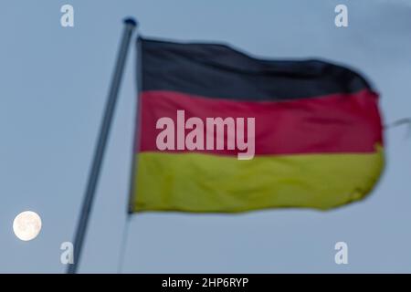 Cottbus, Deutschland. 19th. Februar 2022. Eine vom Wind zerzauste deutsche Flagge fliegt auf einem Fahnenmast. Im Hintergrund der abnehmende Mond Quelle: Frank Hammerschmidt/dpa/Alamy Live News Stockfoto