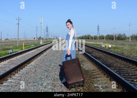 Junge Frau mit Koffer auf Schienen der Eisenbahn. Sommerurlaub und Reisekonzept. Stockfoto