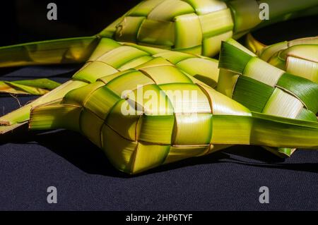 Ketupat, auf dunklem Hintergrund, ein Reiskuchen, der in einem diamantförmigen Behälter aus Kokosblättern verpackt ist Stockfoto