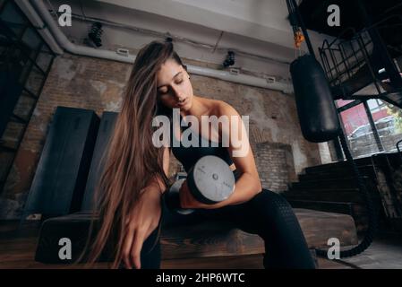 Junge Frau pumpt die Muskeln mit einem Arm Hantel heben. Stockfoto