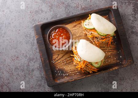 Köstliche gedämpfte bao-Brötchen-Sandwiches mit gezogenem Schweinefleisch aus nächster Nähe auf einem Holztablett auf dem Tisch. Horizontale Ansicht von oben Stockfoto