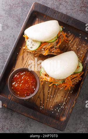 Gedämpftes bao-Brötchen gefüllt mit Pulled Schweinefleisch und Gemüse köstliche Gourmet-Snack in der Nähe in der Holzbrett auf dem Tisch. Vertikale Draufsicht von oben Stockfoto