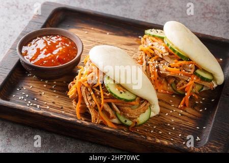 Street Food bao Sandwiches mit gezogen Schweinefleisch und Gemüse Nahaufnahme auf einem Holztablett auf dem Tisch. Horizontal Stockfoto