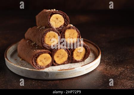 Stapel veganer Schokoladencrepes mit Banane auf dunklem Hintergrund Stockfoto