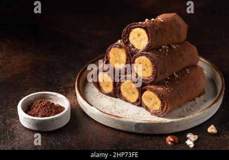 Gerollte Schokoladencrepes mit Banane und Nüssen auf dunklem Hintergrund Stockfoto