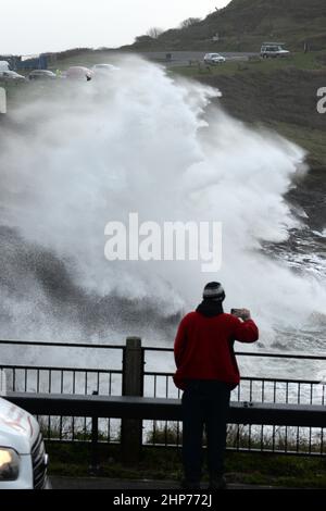 Die Mumbles .18th Feb. 2022 Wellen ragen die Klippen hoch, während ein Passant in Limeslade, Mumbles, Swansea, Wales, Großbritannien, für ein Foto hält. Stockfoto