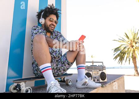 Hispanischer Mann, der Spaß mit dem Smartphone hat und am tropischen Strand Musik hört Stockfoto