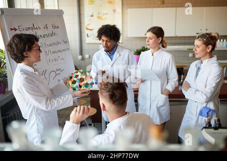 Junge Chemiestudenten hören einem Dozenten im Universitätslabor in einer Arbeitsatmosphäre aufmerksam zu, während sie einen Kurs absolvieren. Wissenschaft, Chemie, Stockfoto