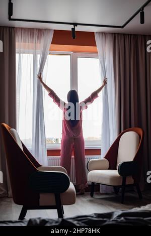 Rückansicht Morgenfrau im Schlafanzug Vorhänge öffnen Blick auf Fenster genießen neuen Tag im Schlafzimmer Stockfoto