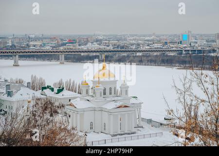 Seminary Church of Alexis, Metropolit von Moskau am Ufer des Flusses Oka, Nischni Nowgorod. Winterliches Stadtbild, gefrorener Fluss. U-Bahn-Brücke im Hintergrund Stockfoto