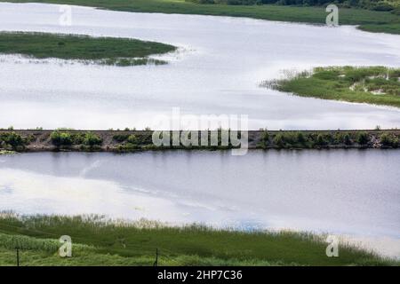 Böschung mit Bahngleisen, die entlang der Wasseroberfläche des Sees führen. Stockfoto