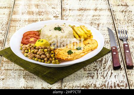 Reis mit brasilianischen Bohnen, serviert mit Salat, gebratenem Hühnerfilet und Farofa. Serviert auf einem rustikalen Tisch Stockfoto