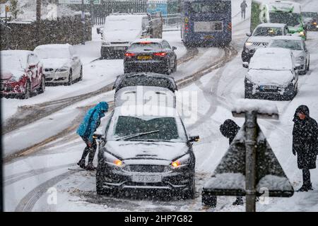 Schnee und Eis verursachen Störungen auf den Hügeln um Bradford, West Yorkshire, Großbritannien. 19.. Februar 2022. Autos haben Schwierigkeiten, sich auf rutschigen Winterböden zu bewegen. Frauen versuchen, auf verschneiten Hügeln Räder zu räumen, um ihr Auto in Bewegung zu bringen. Stockfoto