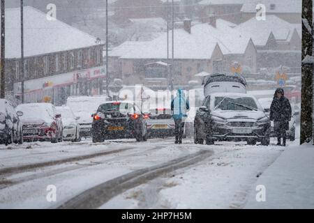 Schnee und Eis verursachen Störungen auf den Hügeln um Bradford, West Yorkshire, Großbritannien. 19.. Februar 2022. Autos haben Schwierigkeiten, sich auf rutschigen Winterböden zu bewegen. Frauen versuchen, auf verschneiten Hügeln Räder zu räumen, um ihr Auto in Bewegung zu bringen. Stockfoto