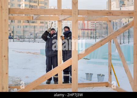 Ein Baumeister in einer blauen Jacke mit einem Hammer in der Hand hämmert einen Nagel Stockfoto