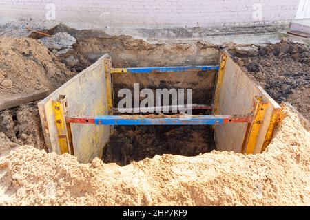 Graben zur Reparatur des Rohrbruchs. Die Wände sind mit Metallstützen verstärkt, um ein Schruppen des Bodens zu verhindern. Stockfoto