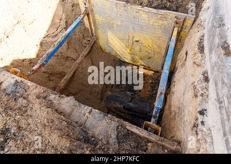 Graben zur Reparatur des Rohrbruchs. Die Wände sind mit Metallstützen verstärkt, um ein Schruppen des Bodens zu verhindern. Stockfoto