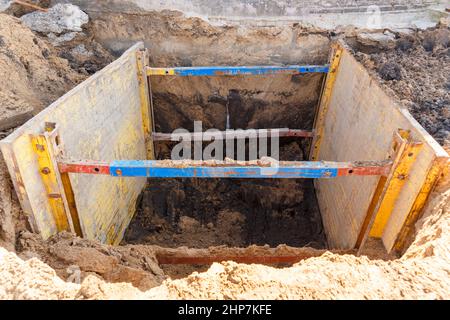 Graben zur Reparatur des Rohrbruchs. Die Wände sind mit Metallstützen verstärkt, um ein Schruppen des Bodens zu verhindern. Stockfoto