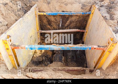 Graben zur Reparatur des Rohrbruchs. Die Wände sind mit Metallstützen verstärkt, um ein Schruppen des Bodens zu verhindern. Stockfoto