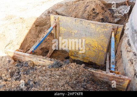 Graben zur Reparatur des Rohrbruchs. Die Wände sind mit Metallstützen verstärkt, um ein Schruppen des Bodens zu verhindern. Stockfoto