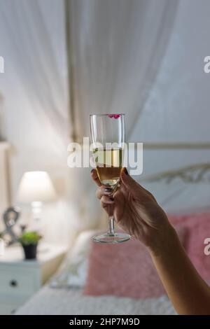 Die Hand der Frau hält ein Weinglas. Im Hintergrund ist ein schönes Zimmer. Stockfoto