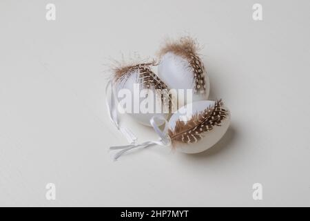 Weiße ostereier sind mit einer Feder verziert. Eier stehen auf einem weißen Tisch. Stockfoto