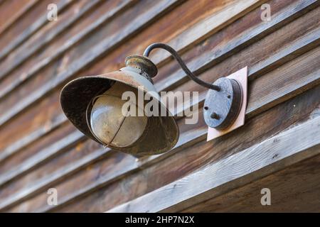 An der Holzwand der Scheune ist eine alte Metalllampe mit einer Abdeckung befestigt. Stockfoto