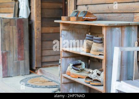 Holzregale vor dem Haus auf dem Bauernhof, in dem sich alte Schuhe befinden. Stockfoto