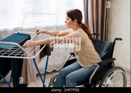 Kaukasische Frau im Rollstuhl hängt nasse Wäsche an einem Trockner. Stockfoto