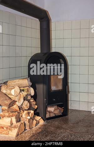 Kamin in der Ecke des Zimmers und neben dem Ofen ist Holz zum Heizen gestapelt. Stockfoto