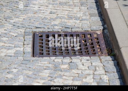Kanal für die Regenwasserableitung in den Abwasserkanal. Der Kanal wird in den Pfad der Pflastersteine eingeführt. Stockfoto