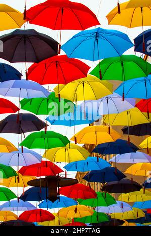 Über der Straße in der Luft hängen unterschiedlich farbige Schirme. Stockfoto