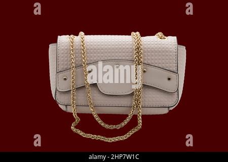 Kleine beige Damen-Handtasche mit einer goldenen Kette. Foto auf dunklem Hintergrund. Stockfoto