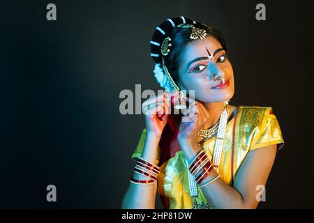 Indische bharatanatyam-Tänzerin, die Ohrringe trägt, indem sie die Kamera auf der Bühne anschaut - Konzept der Vorbereitung, indische Kultur und Tradition. Stockfoto