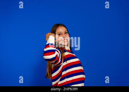 Profilaufnahme einer schönen aufgeregten, ehrgeizigen Dame, die mit einem gestreiften Pullover über dem blauen Studio die Faust hebt und das erfolgreiche Workout feiert Stockfoto