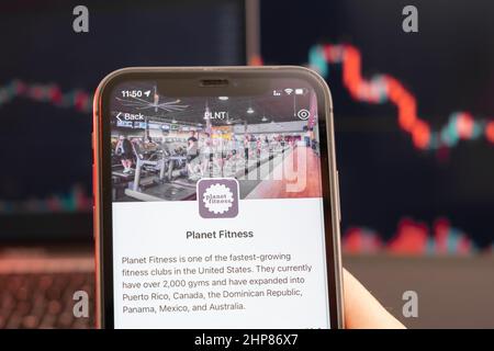 Der Kursrückgang der Planet Fitness-Aktie am Trading-Markt mit einem Balkendiagramm für die Abwärtstrendlinie im Hintergrund. Mann mit Mobiltelefon und Firmenlogo, Februar 2022, San Francisco, USA. Stockfoto