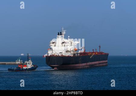 Frachtschiff, das vom Hafen mit Schlepphilfe auf See fährt. Massengutfrachter. Trockenfrachtschiff. Stockfoto