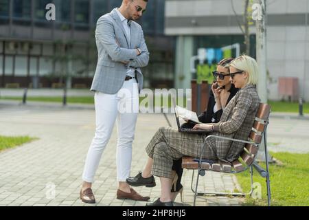 Drei Geschäftsleute arbeiten von außen, während sie auf der Bank sitzen Stockfoto