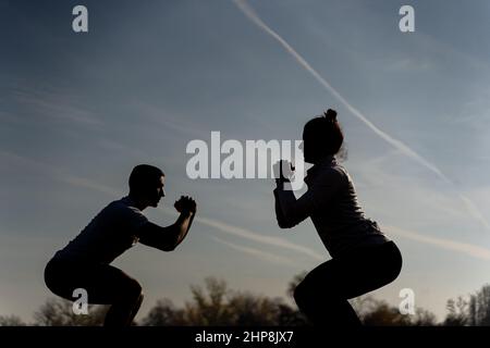 Zwei erstaunliche und attraktive fit Freunde machen Kader-Training auf dem Gras, Silhouette Stockfoto