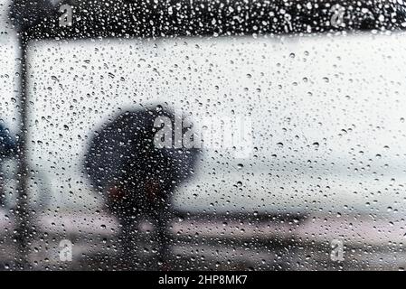 Salvador, Bahia, Brasilien - 15. November 2021: Ein Passagier sitzt an der Bushaltestelle mit einem Regenschirm. Salvador, Bahia, Brasilien. Stockfoto