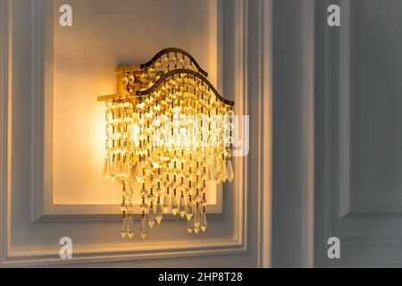 Im Inneren des Zimmers, des Hotels, hängt ein wunderschöner Kristallkronleuchter an einer Wand. Großer Kristall Kronleuchter Glas bricht und reflektiert Licht.klassisch Stockfoto