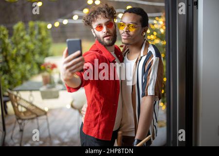 Zwei bunt gekleidete, stylische Jungs, die in Innenräumen Selfie am Telefon machen Stockfoto