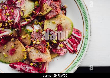 Radicchio Salat mit Wassermelone Rettich, Blutorange, Pistazien auf weißem Teller mit grünem griechischen Schlüssel Stockfoto